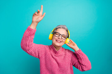 Poster - Photo of overjoyed woman wear pink sweater in glasses enjoy music in headphones raising finger up isolated on teal color background