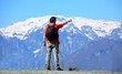 young Man hiker with backpack standing on a mountain trail looking at snowcapped peaks