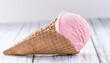 Delicious pink ice-cream in waffle cone on light background. Sweet food. Tasty treat.