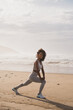 Cheerful fit black woman doing legs stretching exercise at the beach. Healthy and fitness lifestyle. Outdoor workout.