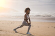 Motivated fit black woman doing legs stretching exercise at the beach. Healthy and fitness lifestyle. Outdoor workout.