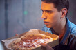 Young calm guy with pepperoni pizza in a cardboard box in the evening in a pizzeria