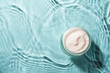 Cream jar in the water on blue background. Top view with copy space.