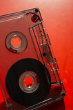 Fototapeta Tęcza - Audio cassette on a blurred red background.