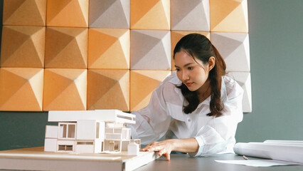 Portrait of professional asian female architect engineer looking while checking at house model at office. Checking real estate house. Business design and building construction concept. Manipulator.