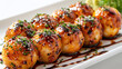 © Photopia - Takoyaki balls garnished with green onion and sauce on a white rectangular plate. Close-up studio food photography. Japanese cuisine and street food concept. Design for menu, poster.
