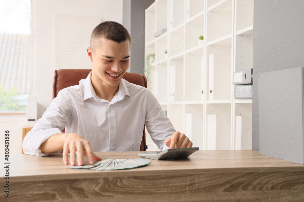 Young man with calculator and dollar banknotes in office