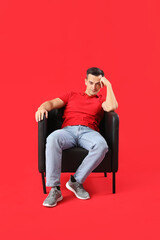 Sticker - Handsome man sitting in black armchair on red background