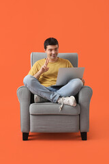 Poster - Young man with laptop video chatting in armchair on red background