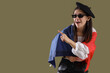 © Pixel-Shot - Young woman in beret and sunglasses pointing with french flag, cultural identity and european travel concept, the woman expresses joy and excitement