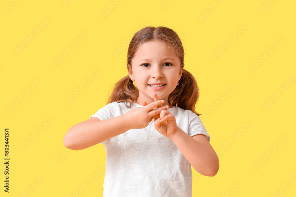 Cute little girl making hashtag gesture on yellow background