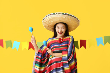 Sticker - Happy young woman in Mexican sombrero hat and poncho holding maracas on yellow background