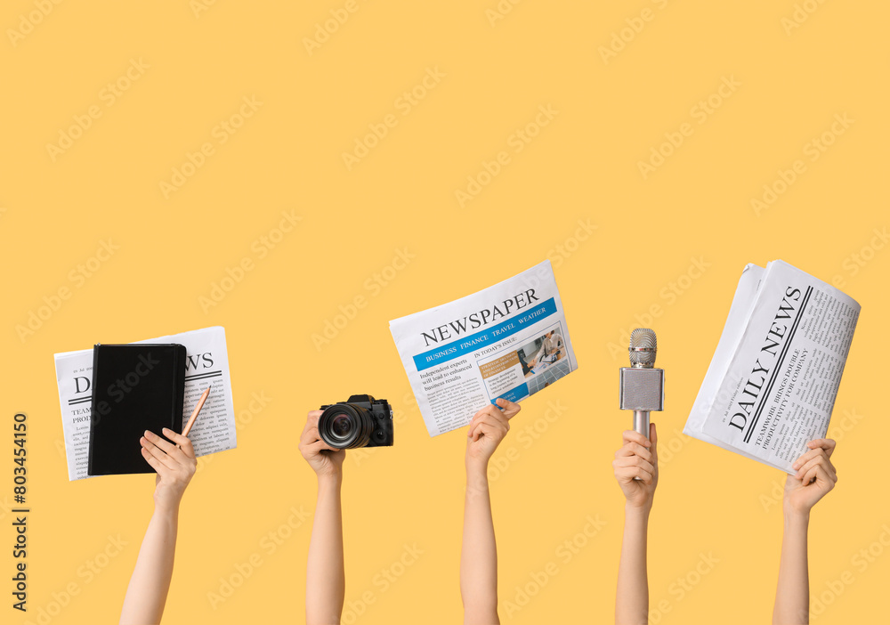 Female hands with newspapers, microphone and photo camera on yellow background