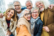 Happy senior people taking selfie picture with smart mobile phone device outside - Old friends having fun together on city street - Technology and aged friendship life style concept