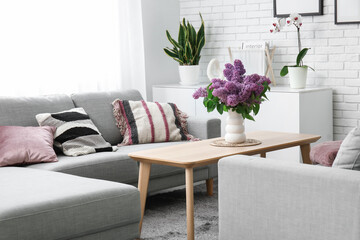 Canvas Print - Stylish interior of living room with bouquet of lilacs branches on coffee table near grey sofas