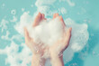 Delicate hands embraced by a voluminous cloud of soap foam, elegantly contrasting with a soothing light blue background.