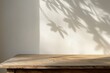 Empty wooden tabletop near white wall with sunlight and shadows from tree leaves. Grunge table countertop template background for presentation and advertisement of products. Mockup