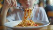 A teenager diving into a plate of spaghetti with gusto, twirling noodles around their fork and slurping up sauce with relish.