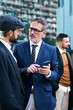 Vertical. Group of Caucasian business men gathered talking serious using and holding mobile phone on break work outdoor. Stylish professional males together conversing quiet outside office building