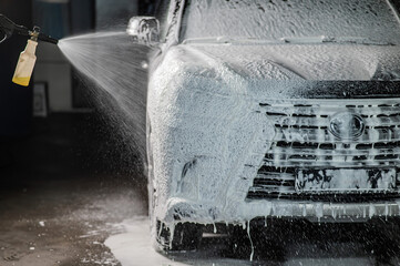 Wall Mural - Man applying foam to black car in car wash. 