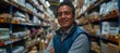 © Денис Никифоров - A portrait shows a Mexican man, employed as a warehouse worker, smiling as he stands surrounded by shelves full of boxes and other equipment in his storage facility.
