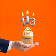 The hand that delivers cupcake with the number 113 candle - Birthday on orange background
