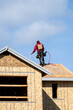 Workman with a nail gun working on roof of new home construction, minimalist image on a sunny spring day
