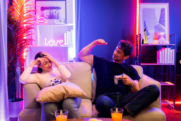 Man winner fighting gamer on video game beside woman loser challenge. Couple joyful playing on TV using joysticks in studio room in red blue neon light bulb at comfy living home place. Postulate.