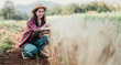 © Satori Studio - Female farmer kneels in the wheat field, taking notes in a notebook, carefully inspecting the crops' development.