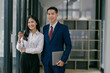© Parichat - A man and woman in business attire stand in front of a window with a cup of coffee