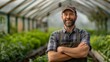 Proud male farmer with arms crossed standing in a greenhouse, surrounded by lush green plants, Concept of sustainable agriculture, organic farming, and local food production