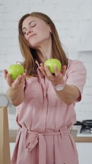 Canvas Print - Beautiful woman in light dress holding green apples. Young happy female with fresh fruit looking at camera in the modern kitchen. Healthy diet. Vertical video