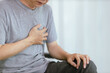 © NanTua - An elderly Asian man having a heart attack sits on a sofa in the living room. The elder clutched his left chest in sharp pain. heart attack symptoms, difficulty breathing