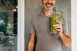 © Maskot - Midsection of smiling man holding glass of fresh green smoothie against wall at resort