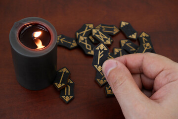 Wall Mural - Burning candle and many wooden runes on table. Human hand shows rune fehu.