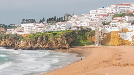 Wall Mural - Wide sandy beach and Atlantic ocean in city of Albufeira timelapse. White houses on the top of cliffs. Elevator from viewpoint to the beach. Aerial view from above. Algarve, Portugal