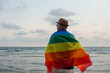 Young asian man with pride movement LGBT holding rainbow flag raise up for freedom. Demonstrate rights LGBTQ celebration pride Month Gay Pride Symbol. Standing on the sand sea beach during sunset