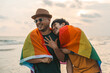 Young couple asian gay with pride movement LGBT holding rainbow flag raise up for freedom. Demonstrate rights LGBTQ celebration pride Month Gay Pride Symbol. Walking on the sand sea beach with sunset
