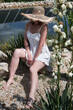 Young sexy beautiful woman in a straw hat is sitting in the garden near lake.