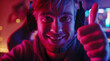 © Vladimir - Gamer celebrates his victory with a thumbs up. Emotional gamer for computer games and game consoles sat in front of the screen. Player with stormy emotions. Neon colors.