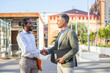 © Guirado - two corporative workers shaking hands outside the office, interracial business team
