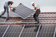 Men technicians carrying photovoltaic solar moduls on roof of house. Electricians in helmets installing solar panel system outdoors. Concept of alternative and renewable energy.