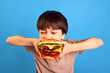 © master1305 - Moment of pleasure. Little boy, kid biting delicious giant burger with meat, vegetables and cheese against blue background. Concept of fast food, childhood, emotions, meal, menu, pop art