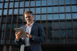 © Stock 4 You - Focused successful mature Indian or Latin entrepreneur businessman holding digital pc tablet standing outdoor at business office building. Hispanic smiling man in suit working using touchpad computer