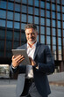 © Stock 4 You - Successful mature Indian, Latin entrepreneur businessman holding digital pc tablet standing outdoor at business office building. Hispanic smiling man in suit working using touchpad computer. Vertical