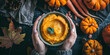 Female hands in sweater holding a bowl with pumpkin soup on dark background. 