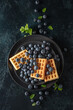 Belgian waffles with blueberries on a black plate.