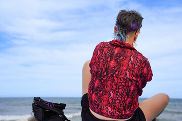 Wall Mural - Back of alternative woman with blue hair and a red and black snake print shirt looking at the horizon
