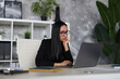© Andrii Zastrozhnov - A pensive Asian businesswoman at her desk, contemplating a problem while working on her laptop.