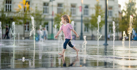 Wall Mural - Cute little boy having fun with water in city fountain. Child playing water games outdoors on hot day. Summer activities for children.